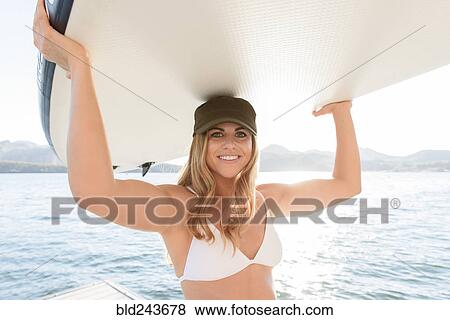 Stock Photo - Hispanic woman carrying paddleboard near river. Fotosearch