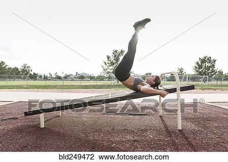 Stock Image - Hispanic woman doing leg lifts outdoors. Fotosearch