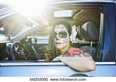 Stock Image - Hispanic woman driving car wearing skull face paint. Fotosearch