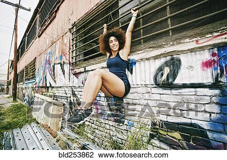 Stock Image - Hispanic woman hanging on bar on graffiti wall. Fotosearch