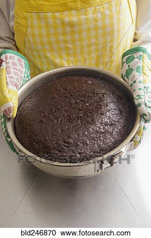 Stock Image - Hispanic woman holding cake in pan with oven mitts. Fotosearch
