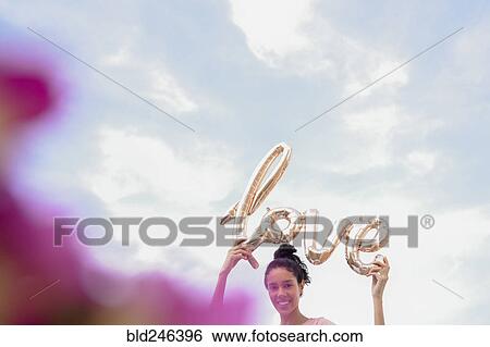 Stock Photograph - Hispanic woman holding love balloon outdoors. Fotosearch