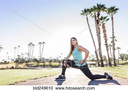 Stock Image - Hispanic woman kneeling and stretching on path. Fotosearch