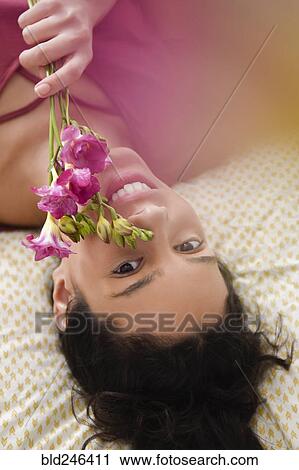Stock Image - Hispanic woman laying on bed holding flowers. Fotosearch