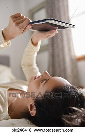 Hispanic woman laying on bed reading digital tablet View Large Photo Image Stock Photo - Hispanic woman laying on bed reading digital tablet. Fotosearch