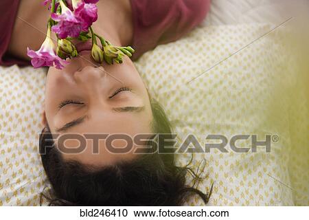 Stock Image - Hispanic woman laying on bed smelling flowers. Fotosearch
