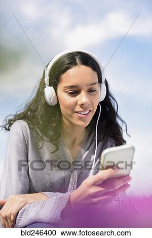 Stock Image - Hispanic woman listening to cell phone with headphones. Fotosearch
