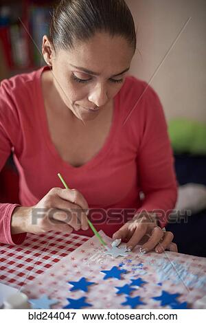 Stock Photo - Hispanic woman painting stars at table. Fotosearch