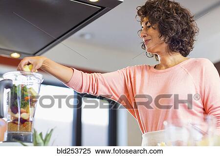 Stock Photography - Hispanic woman preparing smoothie in blender. Fotosearch