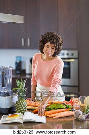 Stock Image - Hispanic woman reading cookbook. Fotosearch