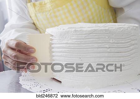 Stock Image - Hispanic woman shaping icing on cake. Fotosearch