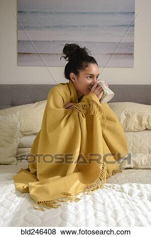 Hispanic woman sitting on bed wrapped in blanket drinking coffee View Large Photo Image Stock Photo - Hispanic woman sitting on bed wrapped in blanket drinking coffee. Fotosearch