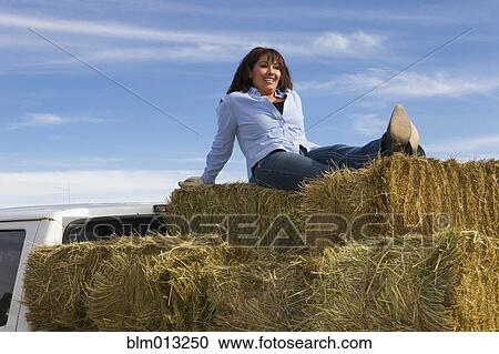 Stock Image - Hispanic woman sitting on hay bales. Fotosearch