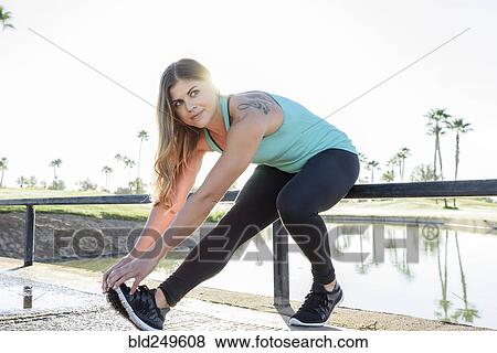 Stock Photo - Hispanic woman stretching leg near pond. Fotosearch