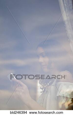 Hispanic woman texting on cell phone behind window View Large Photo Image Picture - Hispanic woman texting on cell phone behind window. Fotosearch