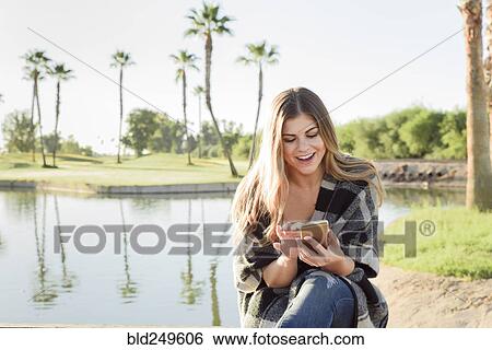 Hispanic woman texting on cell phone near pond View Large Photo Image Stock Photograph - Hispanic woman texting on cell phone near pond. Fotosearch