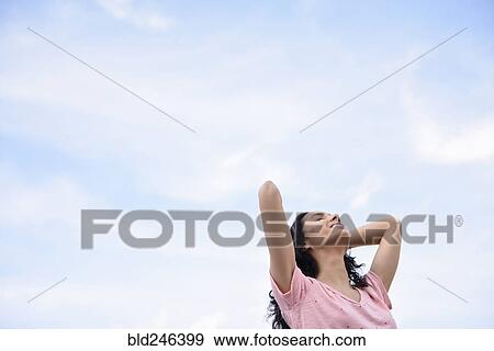 Stock Photo - Hispanic woman with hands in hair under cloudy sky. Fotosearch