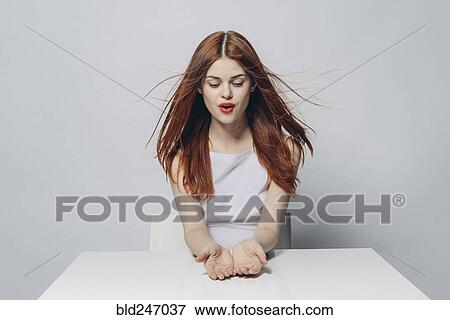 Stock Photo - Hopeful Caucasian woman sitting at windy table. Fotosearch