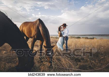Stock Photo - Horses grazing near Caucasian woman hugging cowboy. Fotosearch