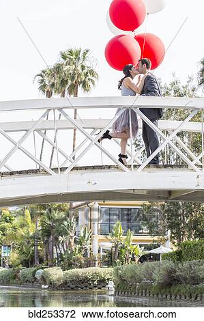 Stock Image - Kissing couple celebrating on bridge with balloons. Fotosearch