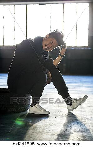 Stock Photography - Laughing androgynous Asian man sitting on wheel. Fotosearch
