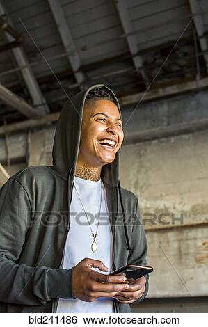 Stock Photograph - Laughing androgynous Mixed Race woman texting on cell phone. Fotosearch