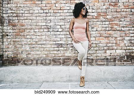 Stock Photo - Laughing Black woman leaning on brick wall. Fotosearch