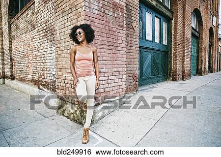 Stock Photograph - Laughing Black woman leaning on corner of brick building. Fotosearch