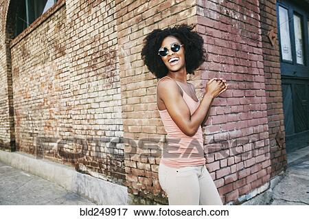 Stock Photo - Laughing Black woman standing near corner of brick building. Fotosearch