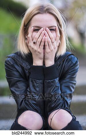 Stock Image - Laughing Caucasian woman covering face with hands. Fotosearch