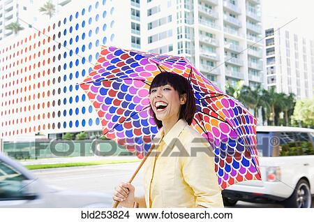 Picture - Laughing Mixed Race woman carrying umbrella in city. Fotosearch