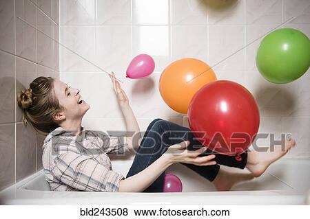 Stock Photo - Laughing woman sitting in bathtub playing with multicolor balloons. Fotosearch