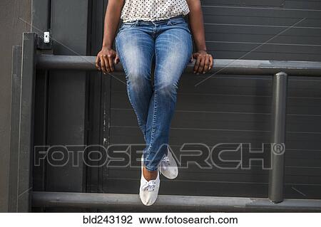 Stock Image - Legs of African American woman sitting on railing. Fotosearch