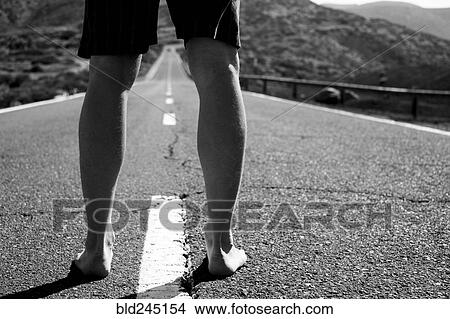 Picture - Legs of barefoot Caucasian man standing in middle of road. Fotosearch