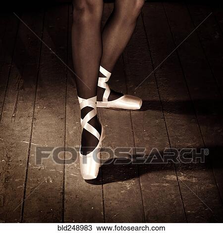 Stock Image - Legs of Caucasian ballerina standing on wooden floor. Fotosearch