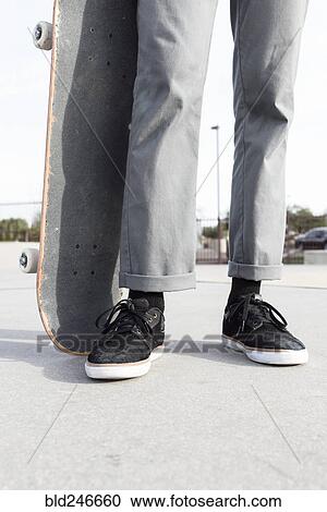 Stock Image - Legs of Hispanic man holding skateboard. Fotosearch