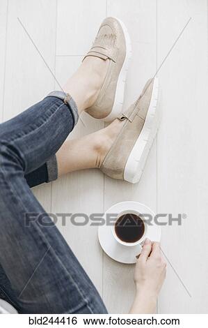 Stock Photograph - Legs of woman sitting on wooden floor drinking coffee. Fotosearch