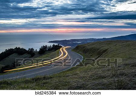 Light trails on winding road near ocean View Large Photo Image Picture - Light trails on winding road near ocean. Fotosearch
