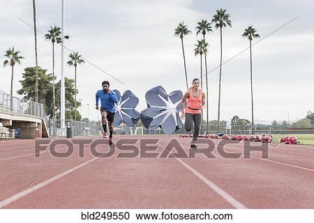 Stock Image - Man and woman running with parachutes on track. Fotosearch