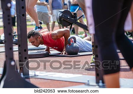 Stock Image - Man doing push-ups near kettlebell outdoors. Fotosearch