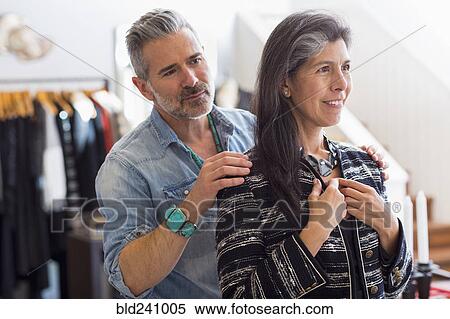 Stock Photography - Man helping woman with jacket in store. Fotosearch