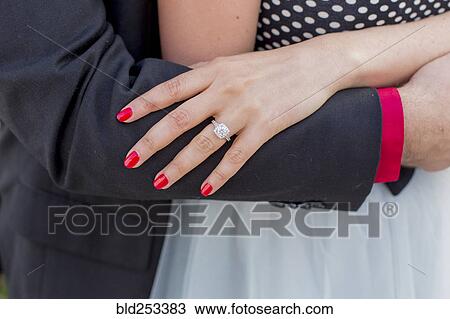 Stock Image - Man hugging woman wearing engagement ring on finger. Fotosearch
