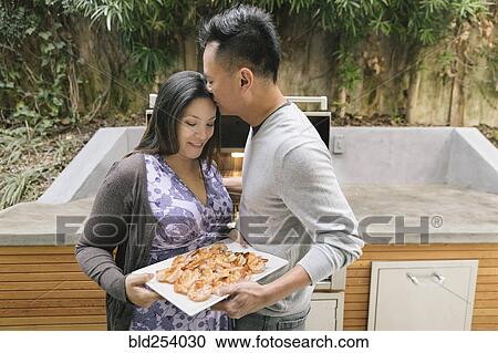 Stock Image - Man kissing forehead of expectant mother near grille. Fotosearch