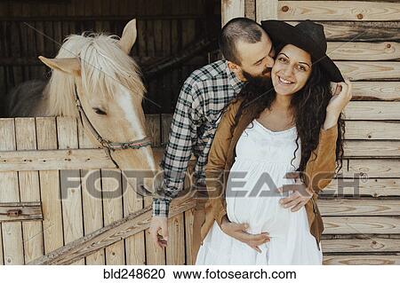Stock Image - Man kissing the woman on cheek near stable. Fotosearch