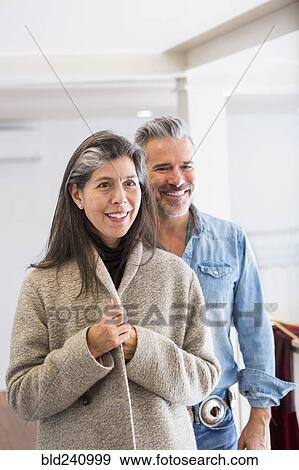 Stock Photo - Man watching woman examining coat in store. Fotosearch