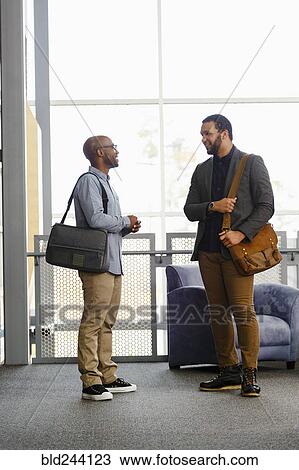 Stock Image - Men carrying briefcases talking in lobby. Fotosearch