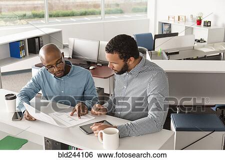 Stock Photograph - Men reading paperwork in office. Fotosearch