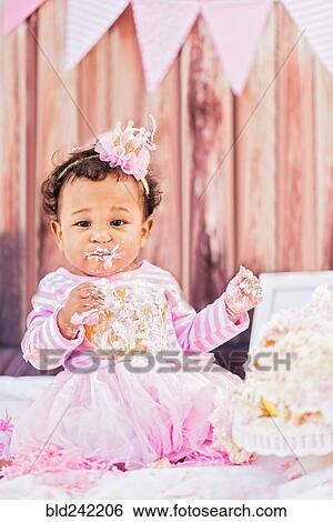 Stock Photograph - Messy Mixed Race baby eating birthday cake. Fotosearch