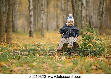 Stock Image - Middle Eastern baby boy sitting on tree stump in autumn. Fotosearch