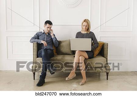 Stock Image - Middle Eastern couple sitting on sofa using technology. Fotosearch